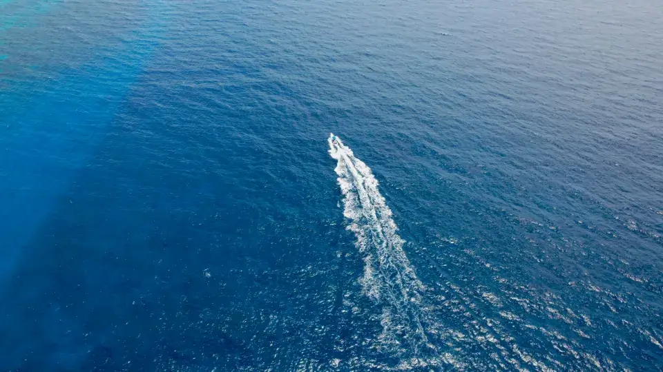 A boat carving a white wake through deep blue open sea, seen from above