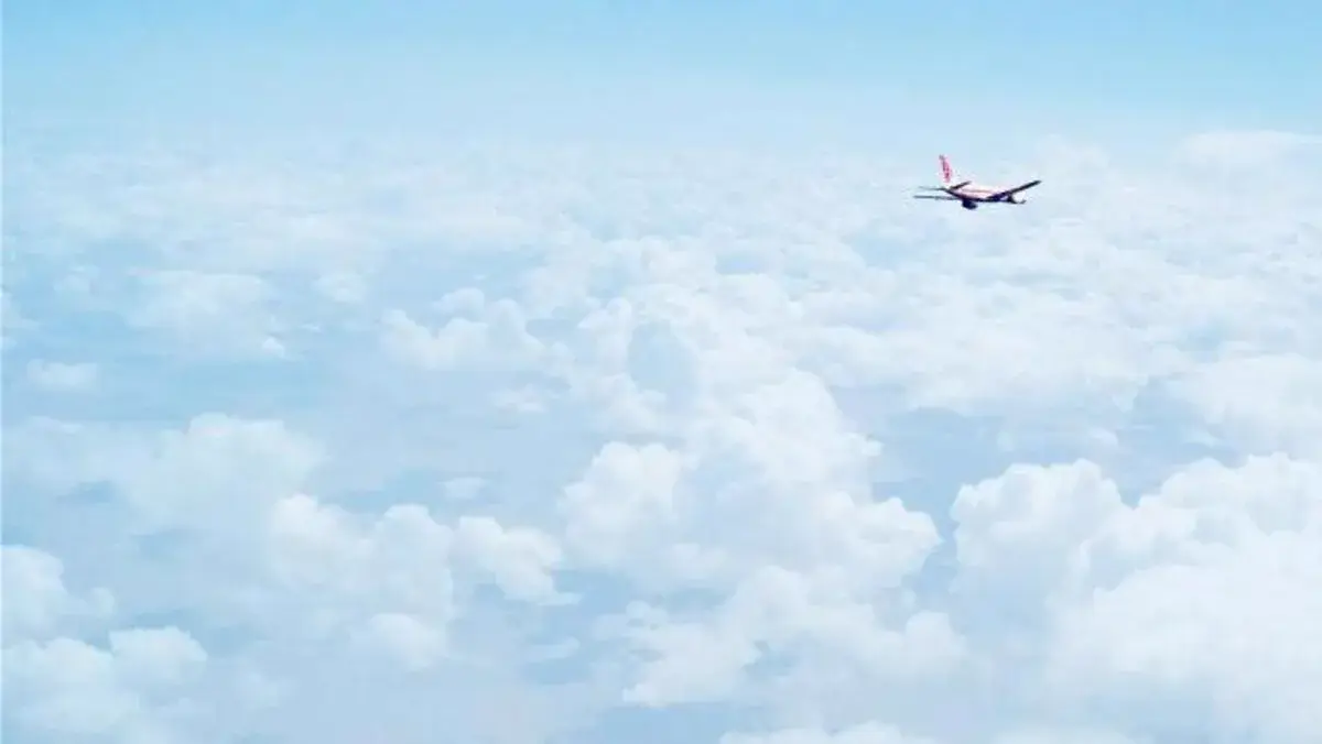 An airliner cruising through bright blue sky above a sea of white clouds