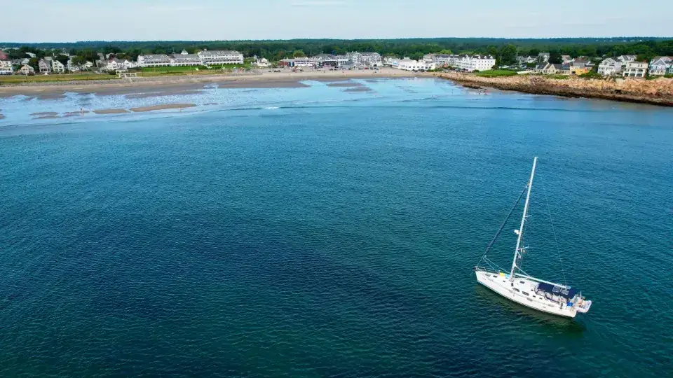 A white sailing yacht on calm turquoise water near a green coastline
